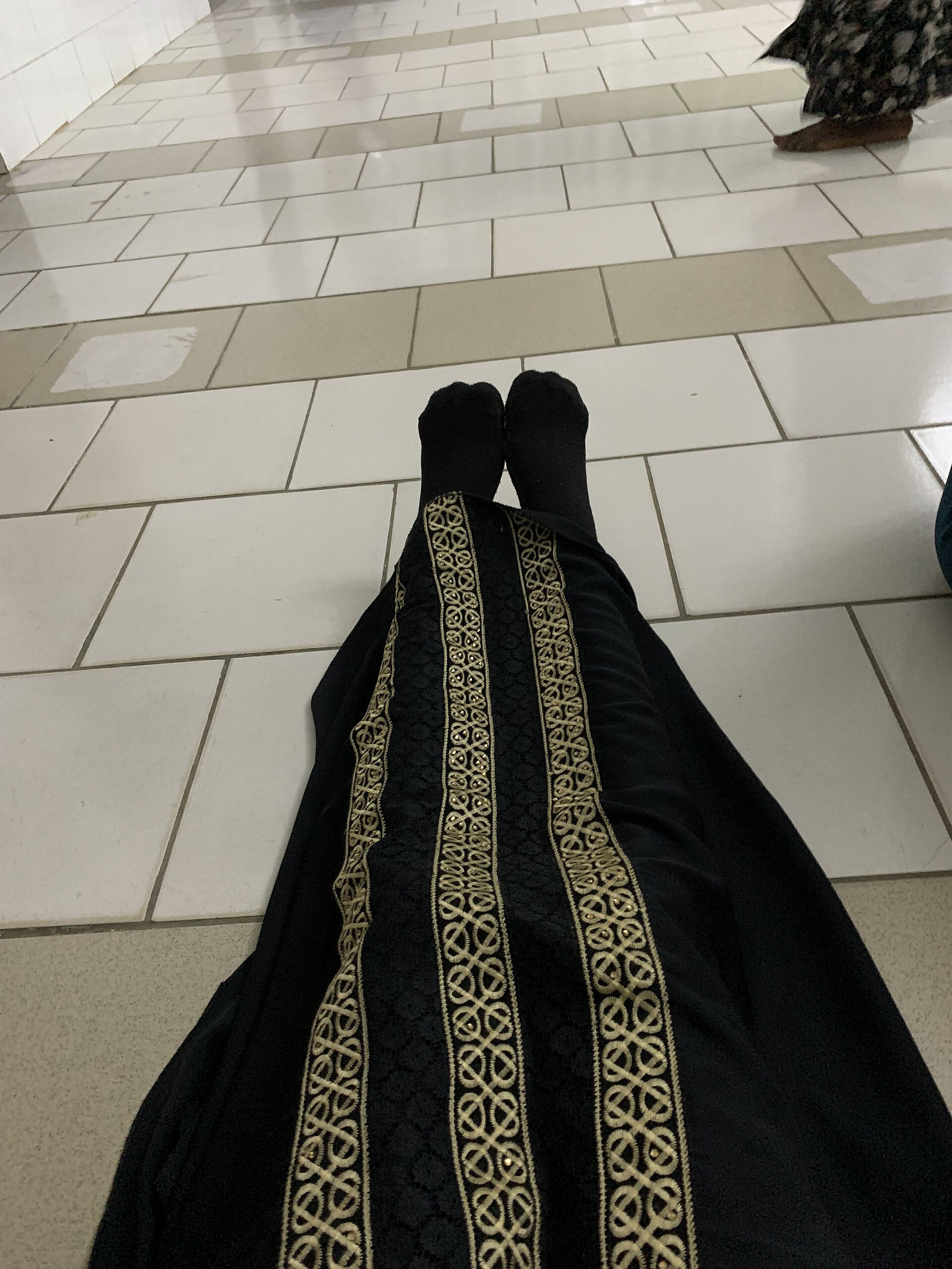 A real black abaya displayed on a mannequin, showing its drape and embroidered front detail
