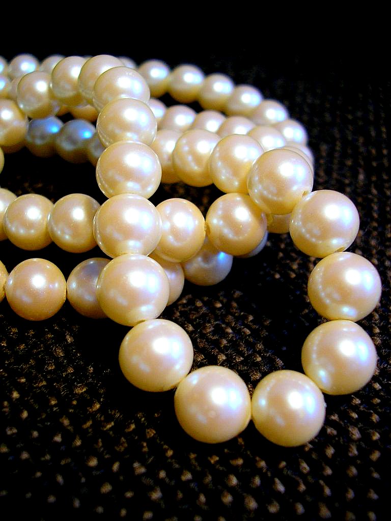 A real white pearl necklace photographed in a loose curve on a dark surface
